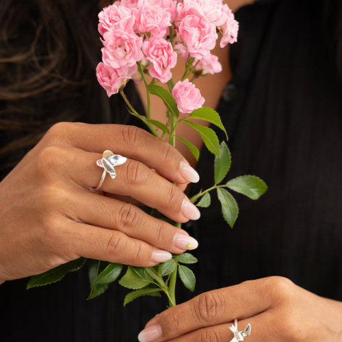 Närbild på händer med Bird Ring och Butterfly Ring i 925 sterling silver från By K Design, med rosa blommor.
