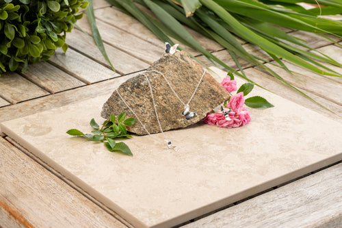 Bird and Butterfly necklace and rings i 925 sterling silver från By K Design, fotograferade med sten och rosa blommor.